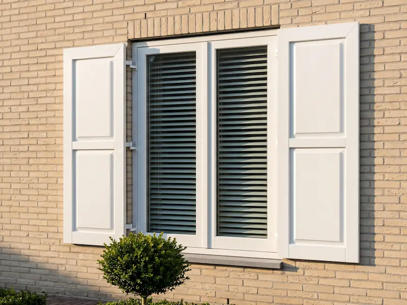 Witte kunststof paneelluiken aan lichte bakstenen gevel — Shutters Inc.